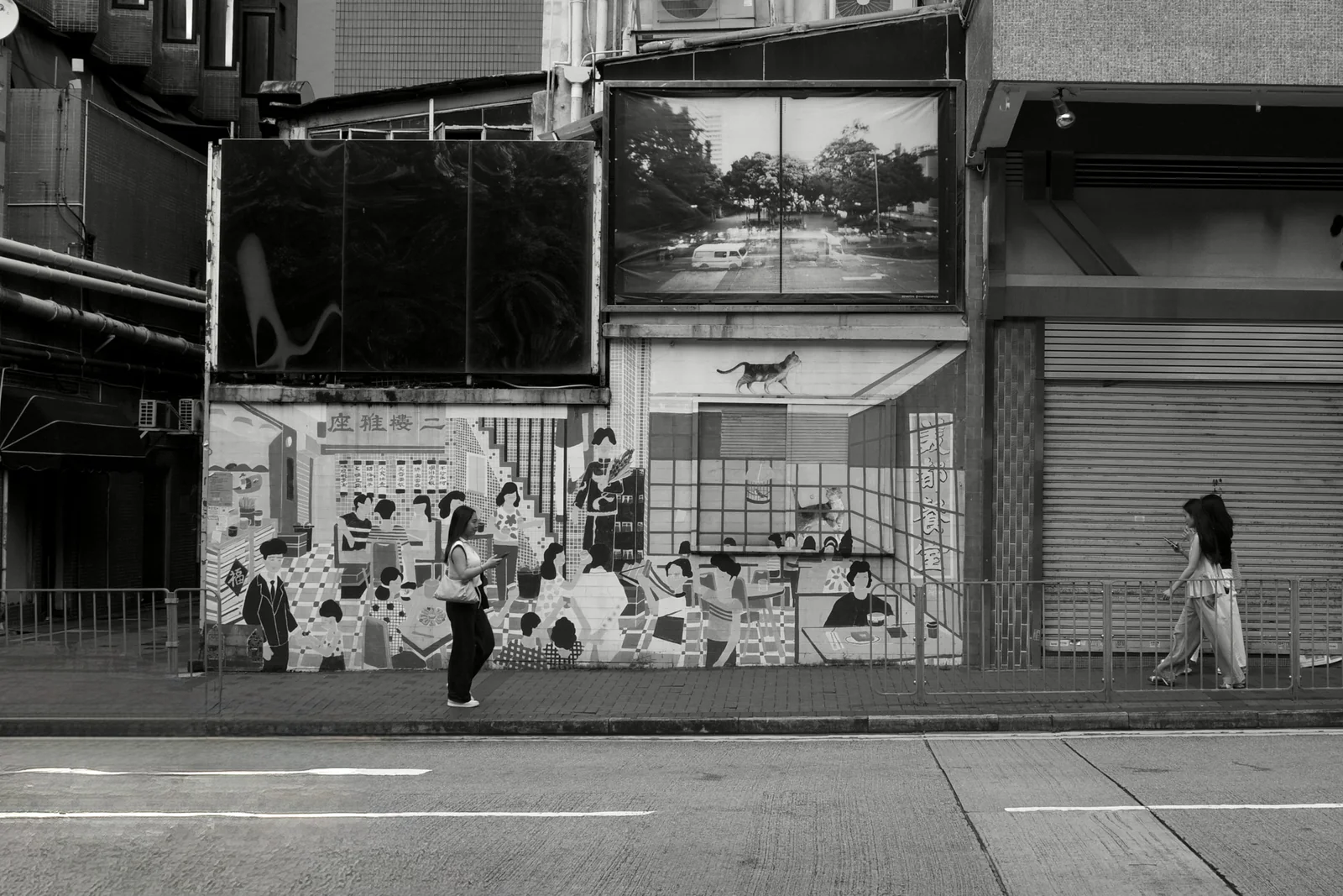 Two women walking past a black-and-white mural of a crowded restaurant scene