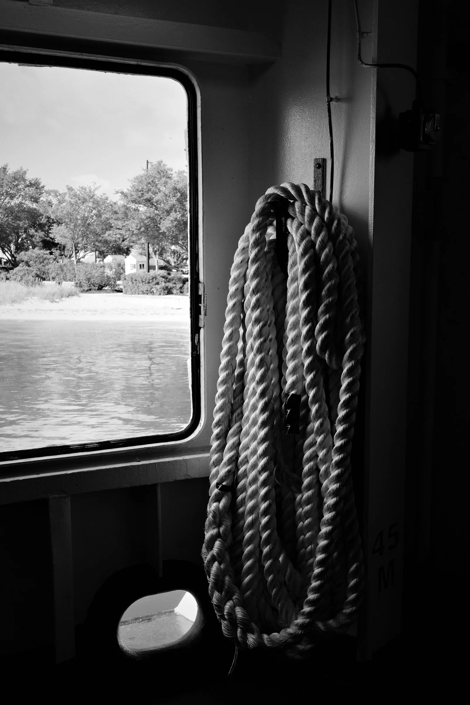 Coiled rope hanging beside a ferry window in black and white