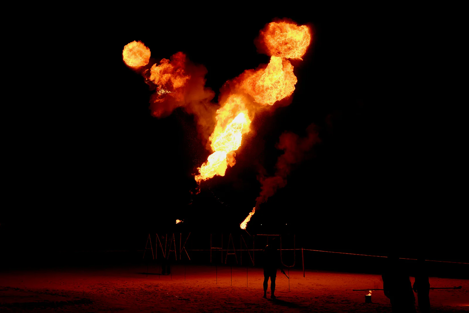 Fire performers silhouetted beneath several bursts of flame at night