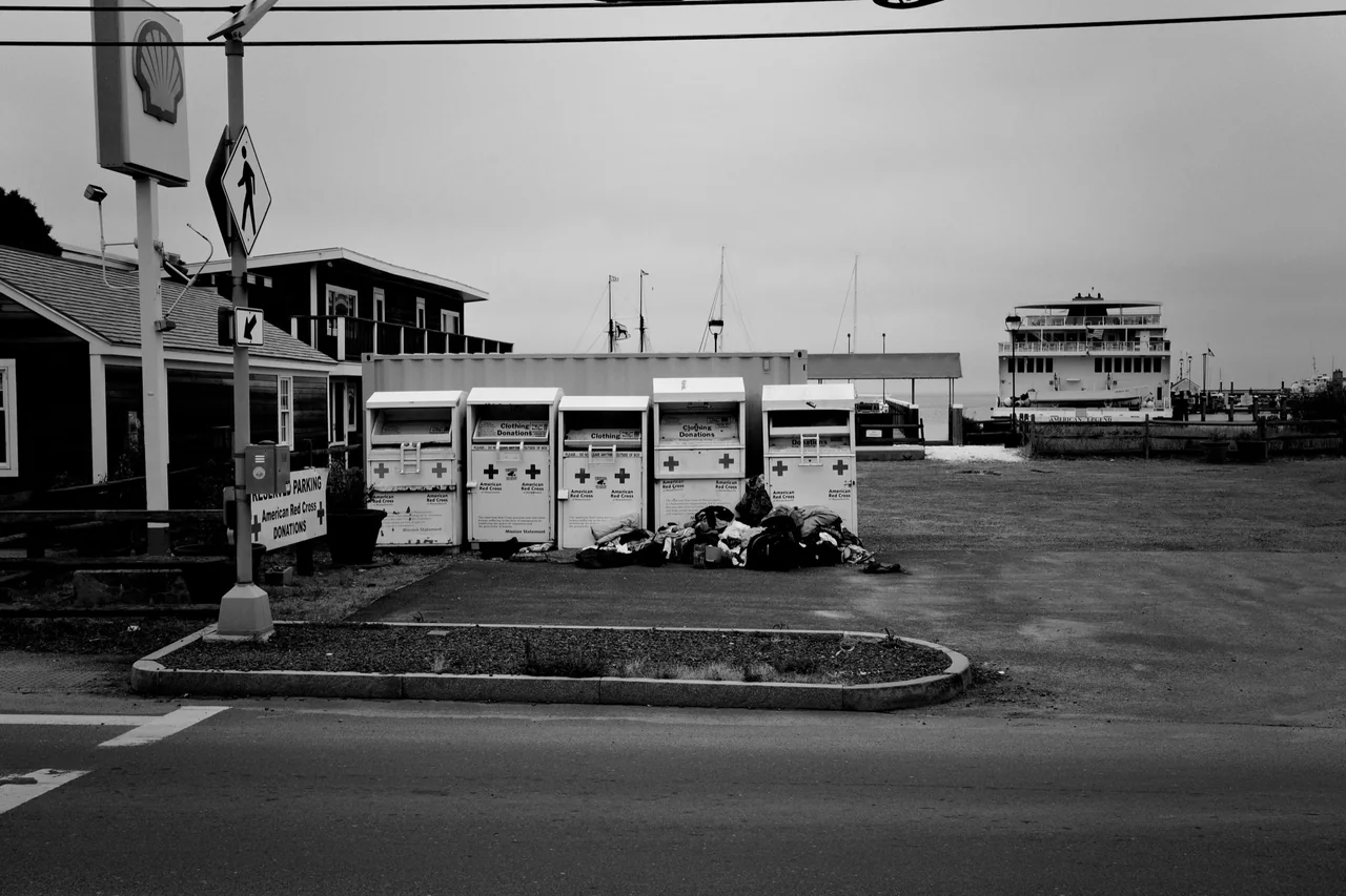 Black-and-white harbor scene with clothing donation bins and a ferry