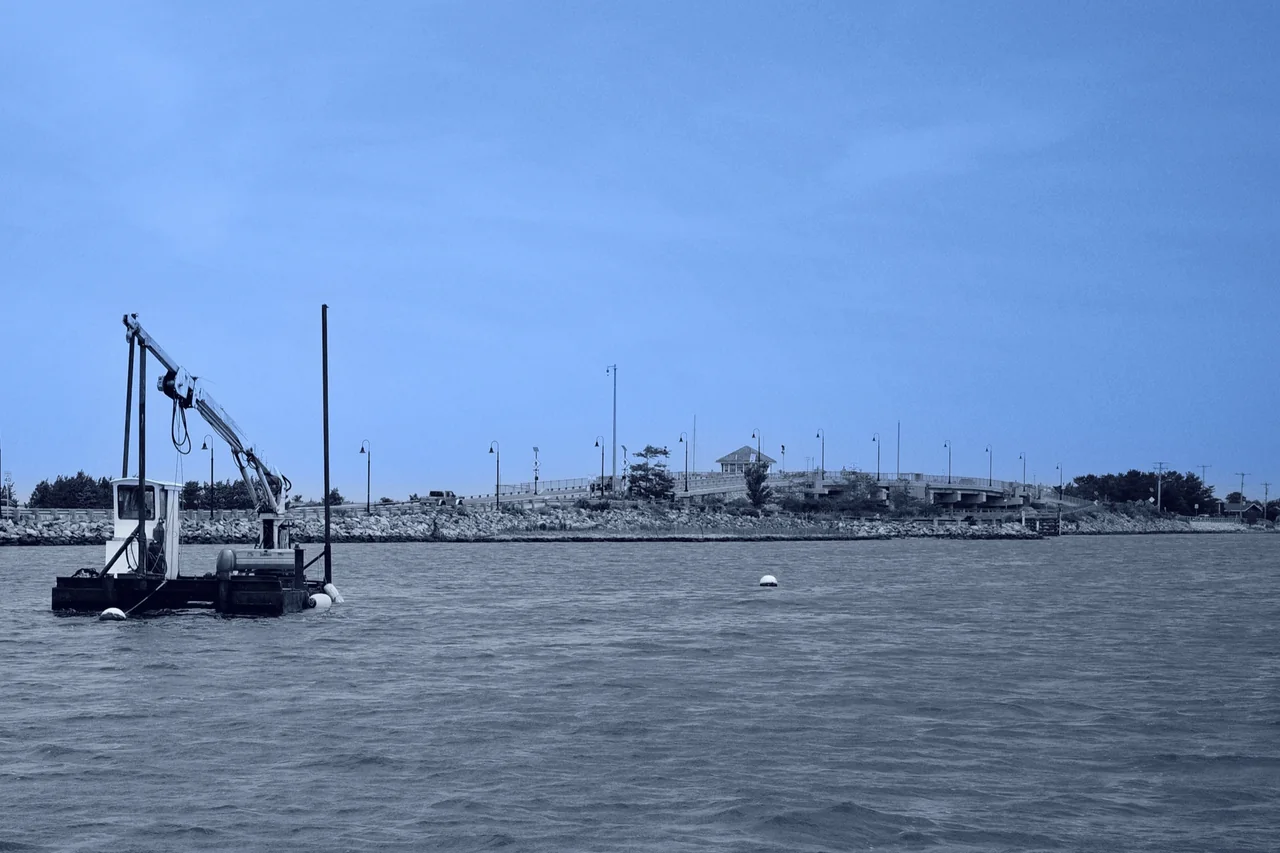 Blue-toned harbor with a workboat, low bridge, and open sky